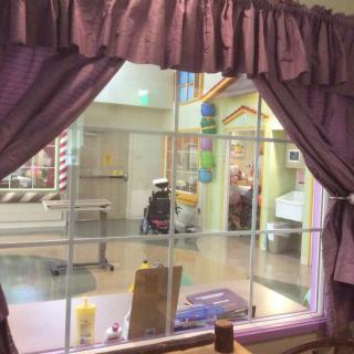View from inside a room with purple curtains looking out to a hospital hallway where a person in a wheelchair is visible.