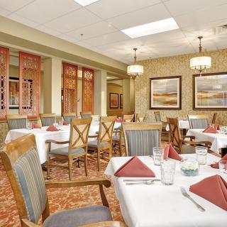Elegant dining room with neatly arranged tables and chairs, featuring warm decor and chandeliers.