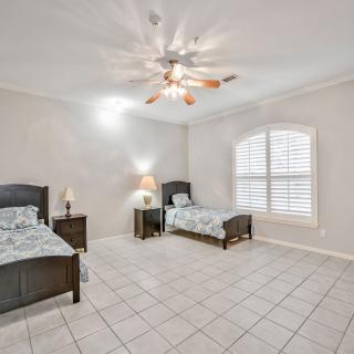 A spacious bedroom with two twin beds, tiled flooring, and a ceiling fan.