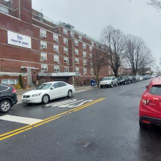 A rainy day view of a residential apartment building with parked cars along the street.