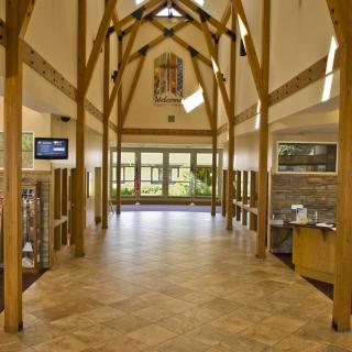 A spacious hallway with wooden beams and large windows, featuring tiled flooring and modern design elements.