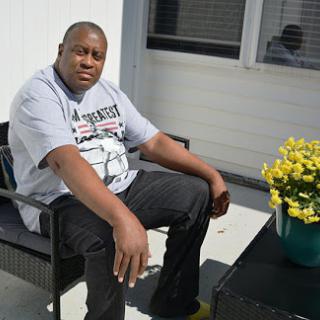 A man relaxing outdoors next to a vibrant flower pot.