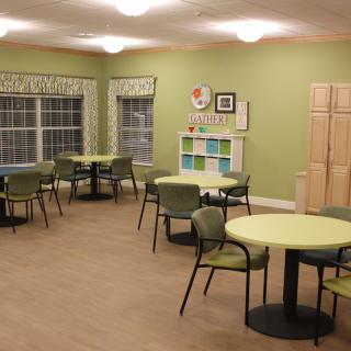 A well-lit dining area with green walls, featuring multiple tables and chairs.