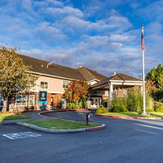 A commercial building with a parking lot and flagpole, set against a partly cloudy sky.