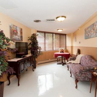 A cozy living room with vintage furniture, a television, and decorative plants by the window.