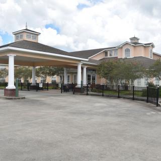 A large, two-story building with a covered driveway and landscaped surroundings under a cloudy sky.