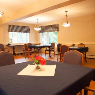 A cozy dining area with neatly arranged tables, decorative flowers, and ample natural light.