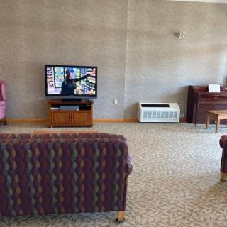 A living room with a television, piano, couch, and armchair.