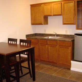 A small kitchen area with wooden cabinets, a dining table, and chairs.