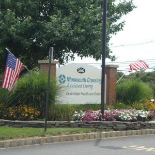 Entrance sign with American flags and landscaped flowers.