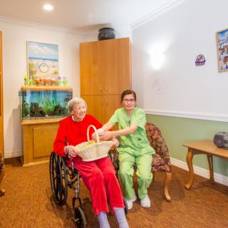 A caregiver assists an elderly person in a wheelchair inside a nursing home.