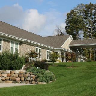 A suburban house surrounded by a well-maintained lawn and trees under a partly cloudy sky.