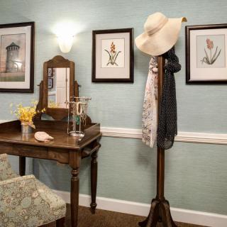 A cozy vintage-style room featuring a vanity table with a mirror and a coat rack adorned with a hat and scarf.