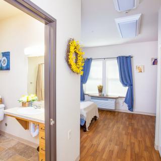 A cozy bedroom with a wooden floor, blue curtains, and a connected bathroom.