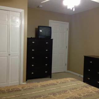A simple bedroom with a dresser topped with a small television, a closet, and a carpeted floor.