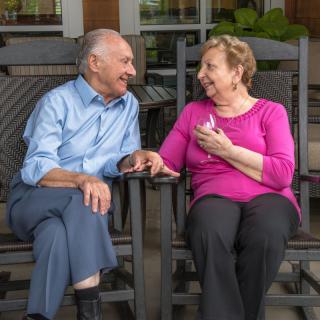 An elderly couple enjoying a conversation while sitting on rocking chairs.