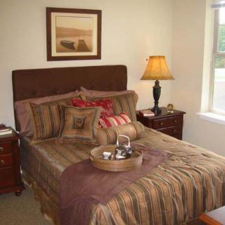 A cozy bedroom featuring a neatly made bed with striped bedding and decorative pillows, complemented by bedside tables with lamps and a window letting in natural light.