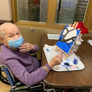 An elderly individual creatively engages in painting while seated in a wheelchair, showcasing their artistic skills.
