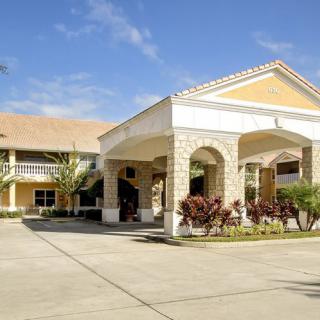 A sunny day view of a residential building with an entrance driveway, surrounded by palm trees.