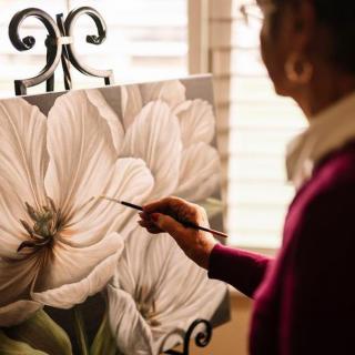 An artist carefully paints a detailed flower on a canvas.