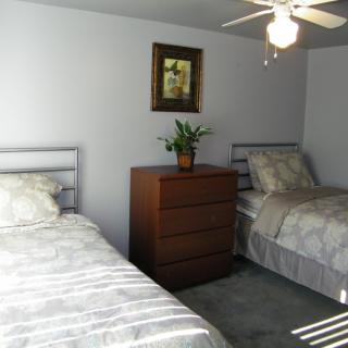 A bright bedroom with two twin beds, a wooden dresser, and a ceiling fan.