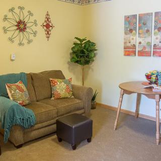 A cozy living room with a sofa, colorful cushions, wall decorations, and a small indoor plant.