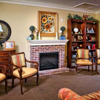 A cozy living room with a brick fireplace, surrounded by comfortable chairs and a decorated bookshelf.