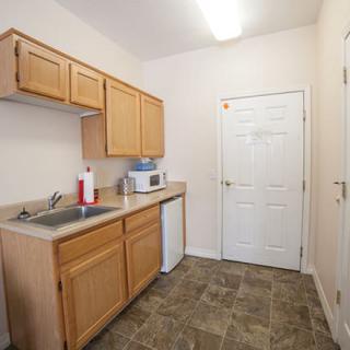 A small kitchen area with wooden cabinets, a sink, and a microwave on the counter.