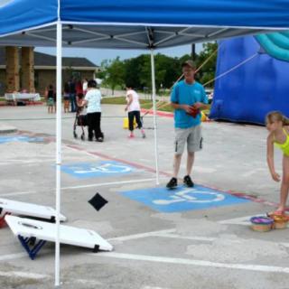 A family-friendly outdoor event featuring games and activities under a tent in a parking lot.