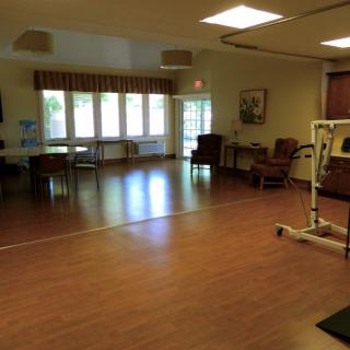 A spacious living area with hardwood floors, featuring chairs and tables under bright lighting.