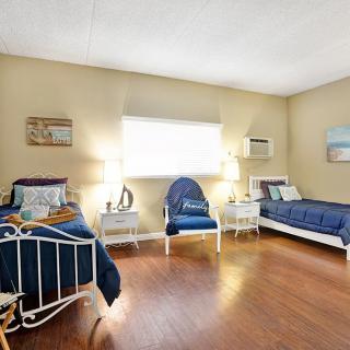 A cozy bedroom with a nautical theme, featuring two single beds adorned with blue bedding, an armchair, and wooden flooring.