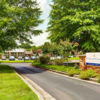 Entrance to a landscaped facility with trees and a sign.