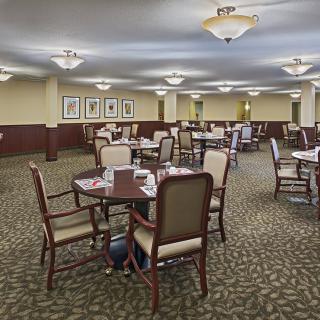An elegant dining room featuring multiple tables and chairs, with soft lighting and carpeted flooring.