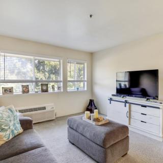 A cozy living room with a sofa, television, and large windows bringing in natural light.