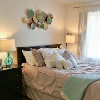 A cozy bedroom with soft lighting, featuring a neatly made bed adorned with multiple pillows and decorative wall art.