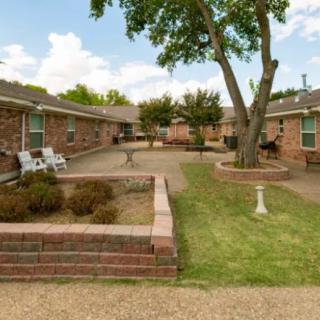 A serene courtyard in an apartment complex with brick buildings, featuring outdoor seating and landscaping.