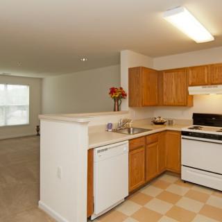 A modern apartment kitchen with wooden cabinets and an open living space.