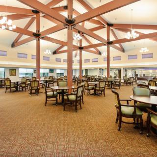 An empty, spacious dining hall with numerous tables and chairs arranged neatly under a high ceiling.