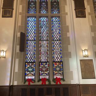 A beautifully designed church interior featuring tall stained glass windows adorned with festive decorations.