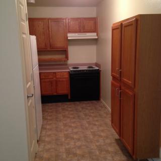 A compact apartment kitchen with wooden cabinets, a stove, and refrigerator.
