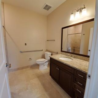 A spacious bathroom featuring a large mirror, vanity with sink, toilet, and overhead lighting.