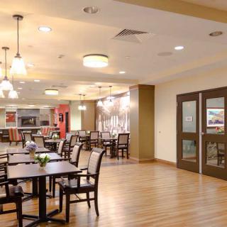 A modern and spacious dining area with wooden flooring, elegant lighting, and neatly arranged tables and chairs.