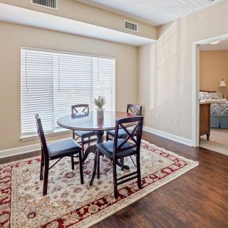 A cozy dining area with a wooden table and chairs, set on a decorative rug, next to a window with blinds.