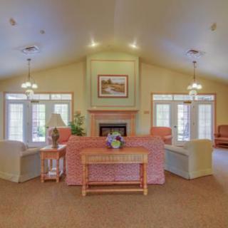 A cozy living room with sofas arranged around a fireplace, adorned with decorative elements and well-lit by natural light from the windows.