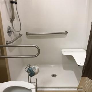 An accessible shower with grab bars, a handheld showerhead, and a folding seat.