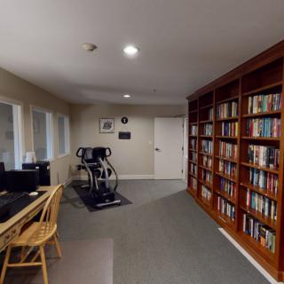 A cozy room featuring a large bookshelf, a treadmill, and a computer desk.