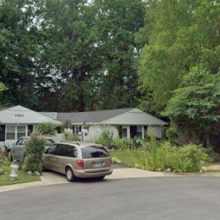 A suburban house with a garden and a car parked in the driveway.