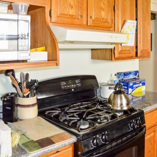 A kitchen featuring a stove with an oven, wooden cabinets, a microwave, and various kitchen utensils on the countertop.