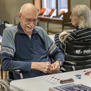 An elderly man and woman seated indoors at a table, engaging in activities and enjoying their time together.