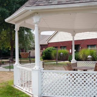 A white gazebo with lattice design in a garden setting, featuring outdoor furniture.